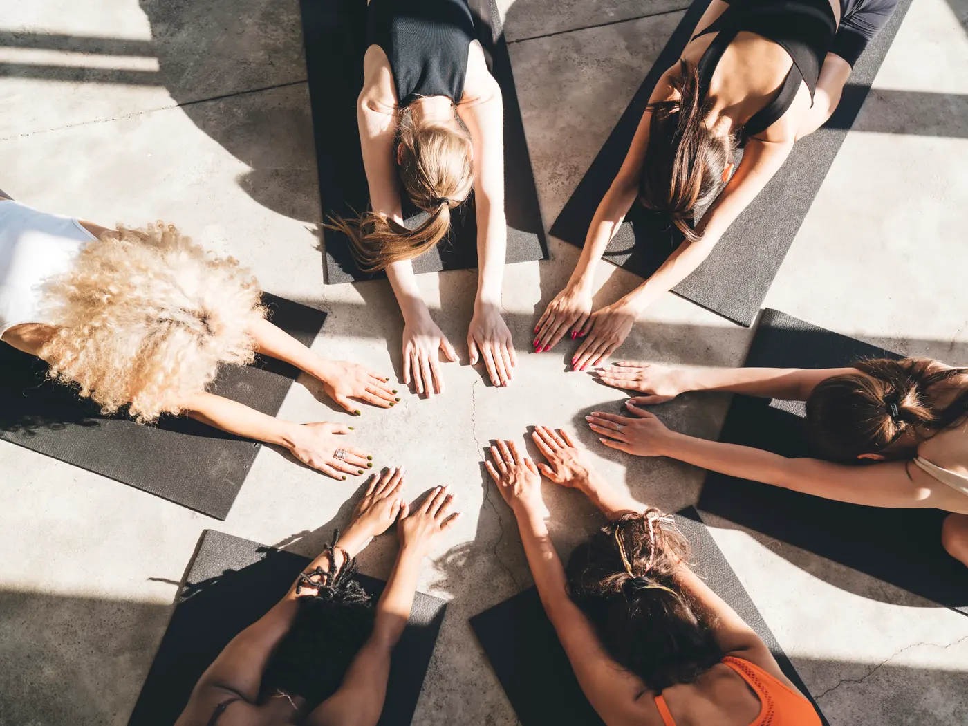 Overhead view of a group yoga class — students gathered in a circle, hands reaching to the centre