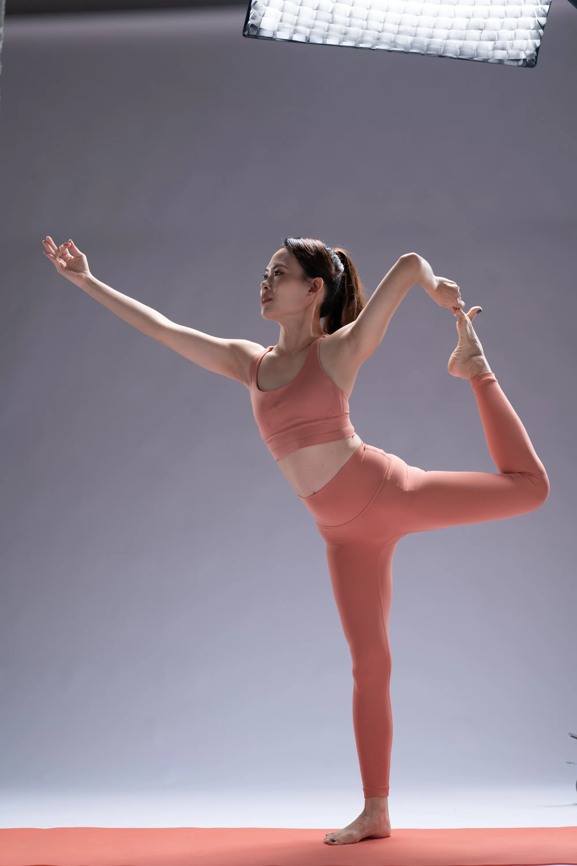 Dr. Jacqueline Yun in dancer pose (Natarajasana), coral practice wear